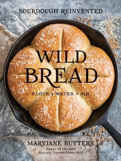 A freshly baked, artisan gluten-free Wild Bread: Sourdough Reinvented Cookbook set in a cast iron pan, sprinkled with flour, embodying rustic charm by Gibbs Smith.