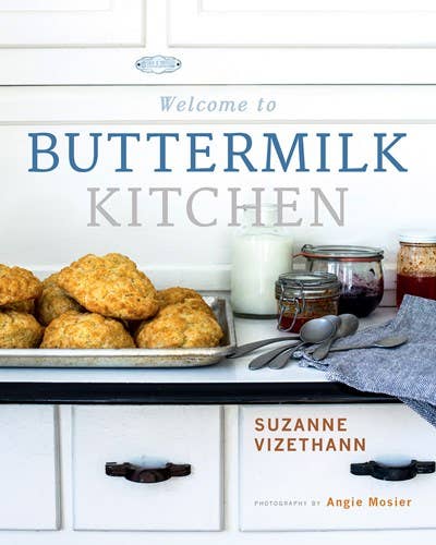 A cozy and inviting cookbook cover titled "Welcome to Buttermilk Kitchen - Cookbook," featuring freshly baked biscuits, a jar of jam, and kitchen utensils on a white cabinet countertop, hinting at delicious recipes.
- Gibbs Smith